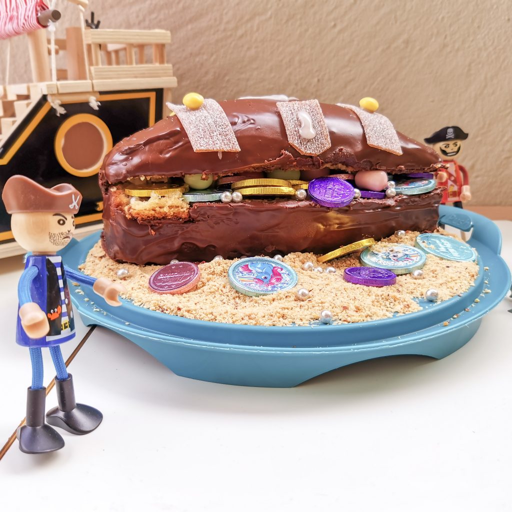Gâteau d'anniversaire en forme de coffre au trésor pirate, rempli de pièces en chocolat et de bonbons colorés.